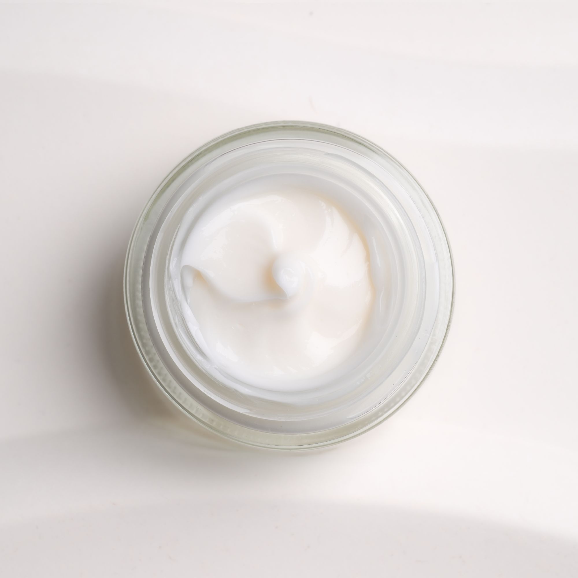 Creme in einem Glas, Draufsicht. Cremige Textur, weiß. Glas mit geriffelter Struktur.