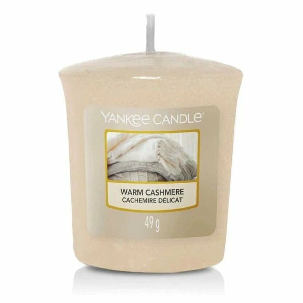 Beige Duftkerze mit Etikett. Aufschrift: Yankee Candle, Warm Cashmere, 49g. Abbildung von Decken. Mit Docht.