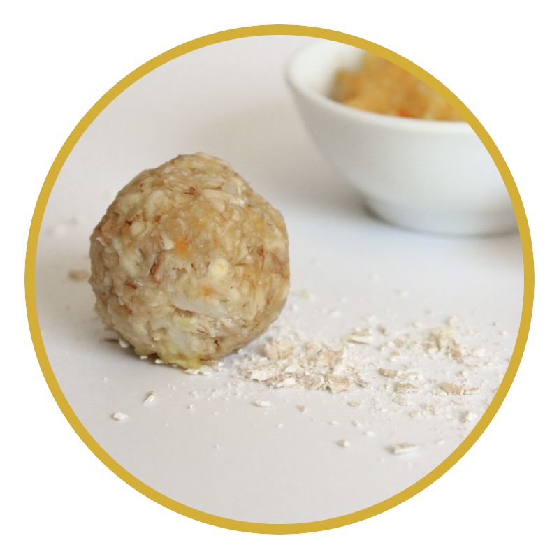 Kugel aus Getreideflocken. Daneben eine Schale mit Fruchtmus. Auf weißem Untergrund. Gelber Kreis.