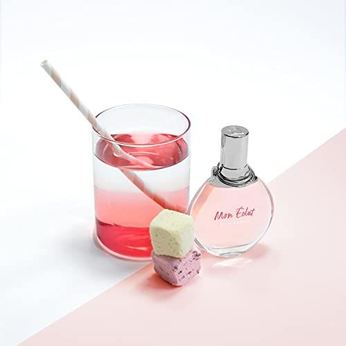 Flakon neben Glas mit rosa Flüssigkeit und Süßigkeiten. Flakon rund, rosa Flüssigkeit. Strohhalm.