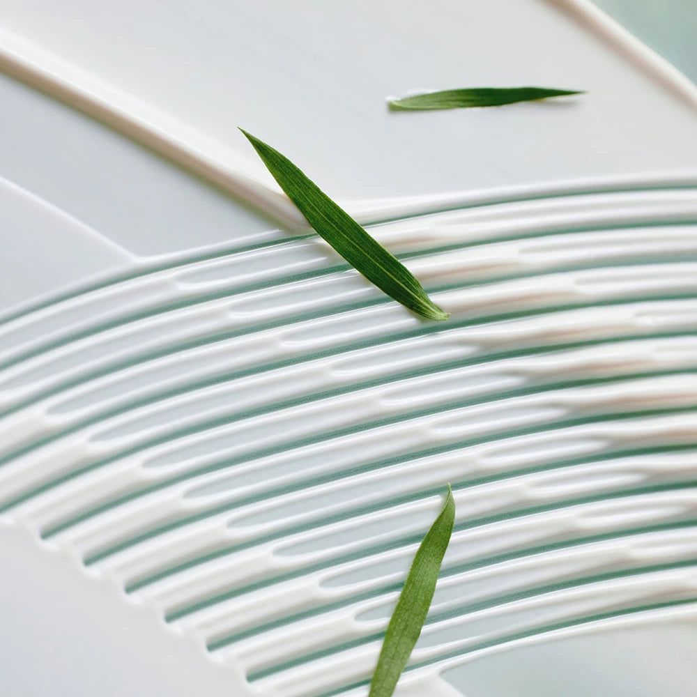 Weißes Produkt mit grünen Blättern. Wellenförmige Textur. Einige grüne Blätter liegen darauf.