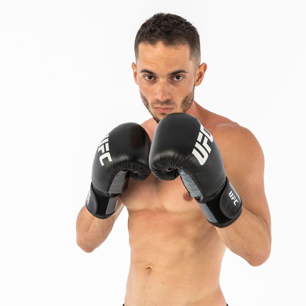 Mann mit schwarzen UFC Boxhandschuhen. Hände in Kampfposition. UFC-Logo auf den Handschuhen.