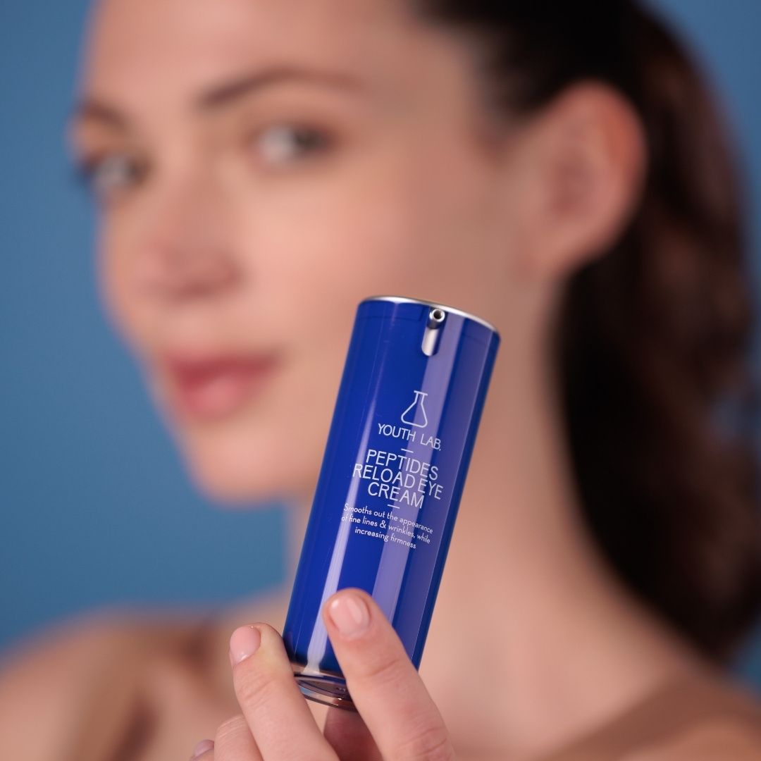 Frau hält blaue Tube. YOUTH LAB Peptides Reload Eye Cream. Text: Glättet feine Linien & Falten, erhöht die Festigkeit.
