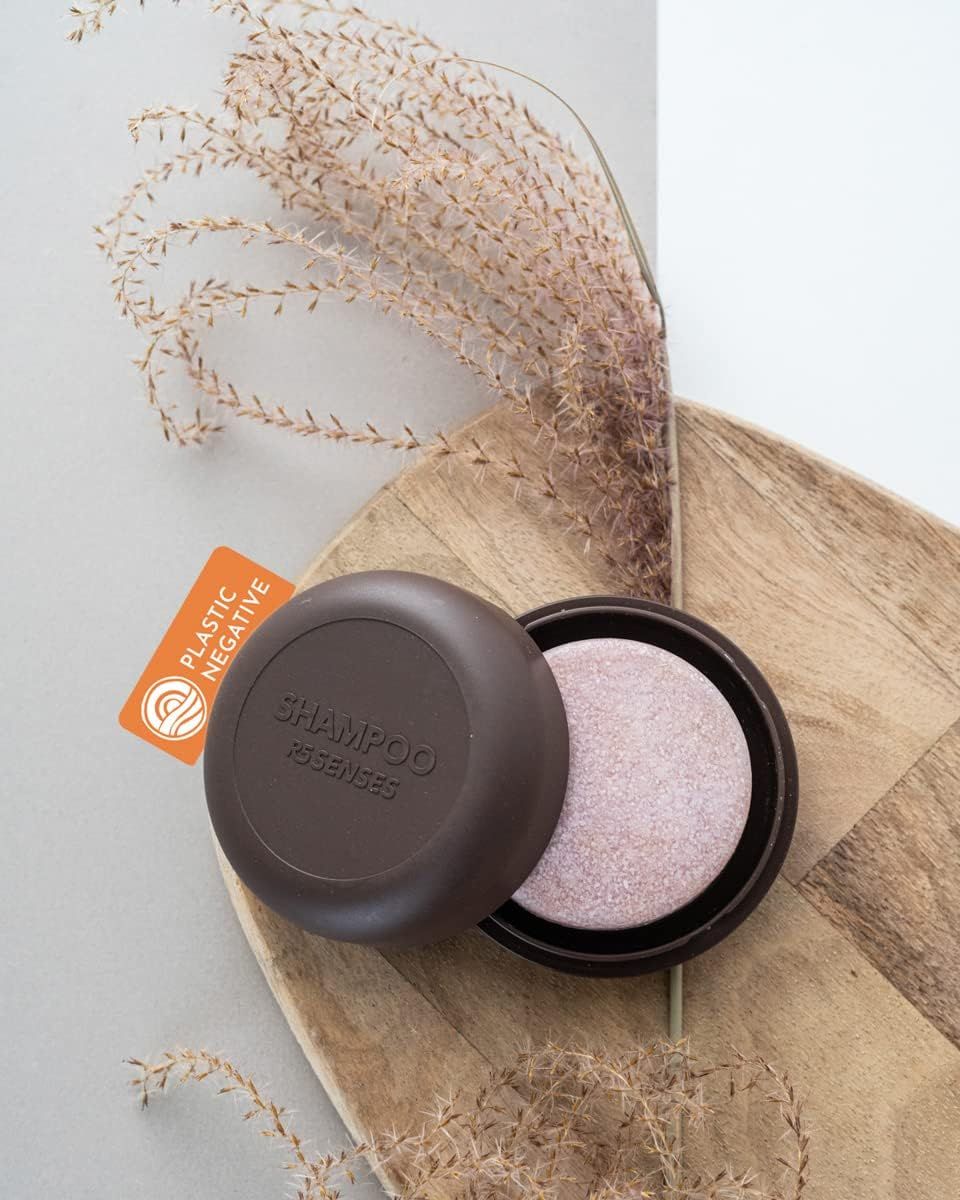 Geöffnete, braune Seifenbox mit Shampoo. Auf Holztablett mit Dekoration. Orangefarbenes Etikett mit Text „PLASTIC NEGATIVE“.