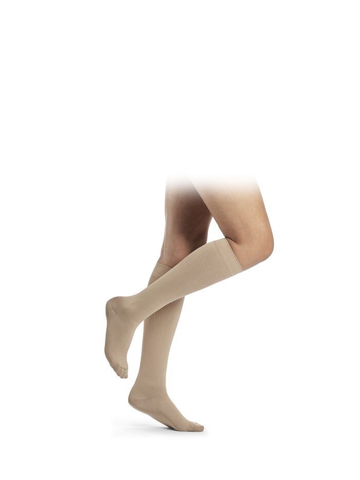 Beige Kniestrümpfe an Beinen. Strümpfe reichen bis unterhalb des Knies. Der Stoff ist glatt und dünn.
