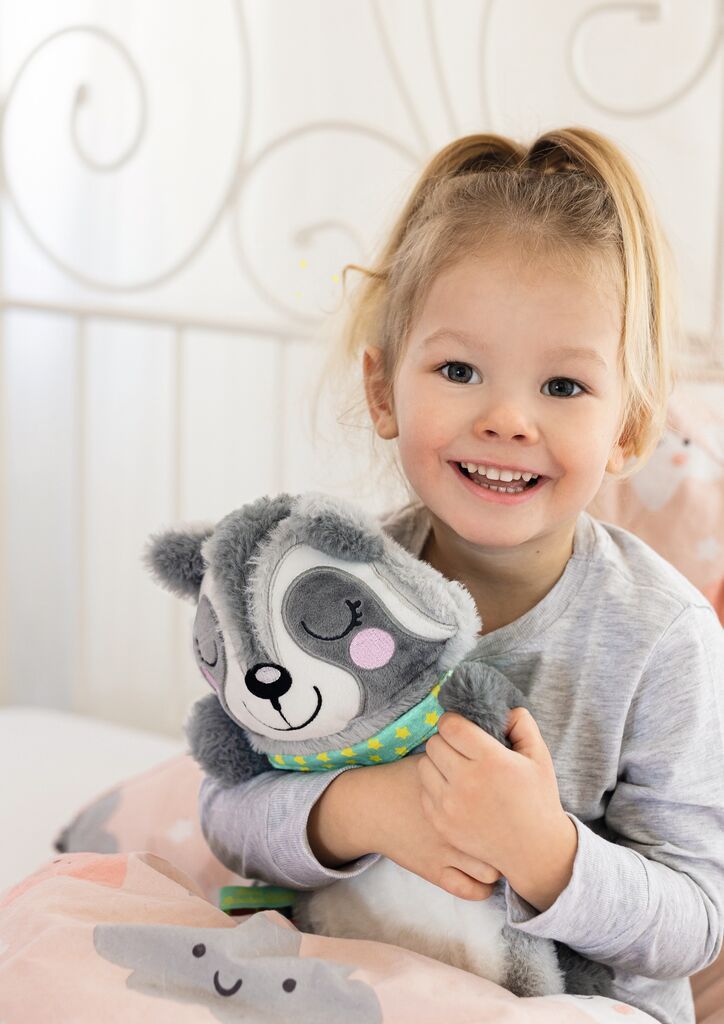 Kleines Mädchen hält einen grauen Waschbär-Wärmflaschenbezug. Das Kind lächelt in die Kamera.