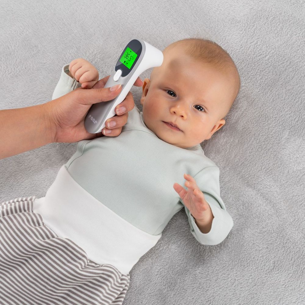 Person misst Temperatur eines Babys mit einem Infrarot-Thermometer. Das Thermometer zeigt 36,5°C an. Marke: reer.
