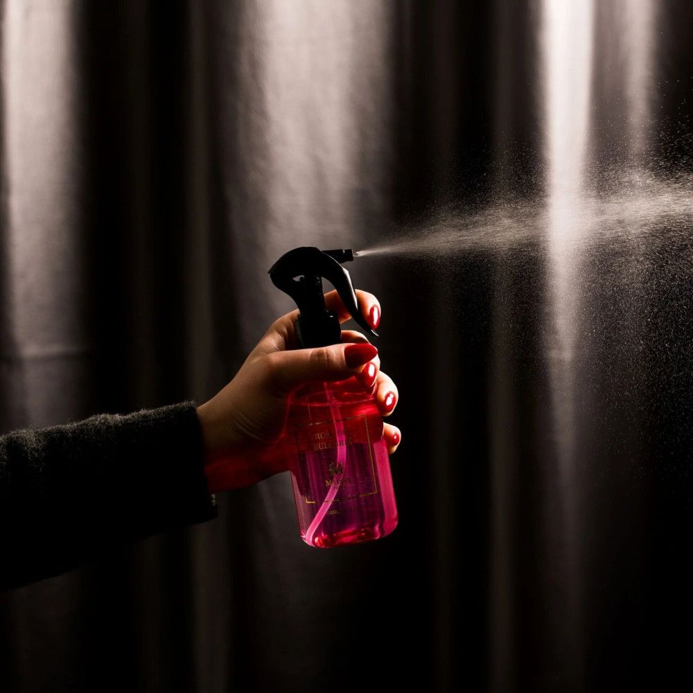 Hand sprüht Flüssigkeit aus rosa Flasche. Schwarzer Sprühkopf. Rote Fingernägel.