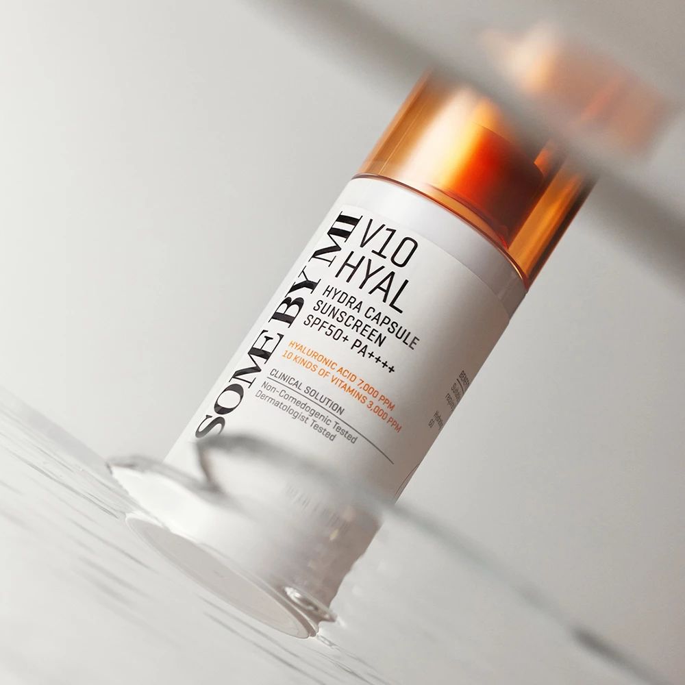 Weißer Flakon mit orangefarbenem Deckel. Aufschrift: V10 Hyal Hydra Capsule Sunscreen SPF50+ PA++++. Flakon im Wasser, leicht unscharf.