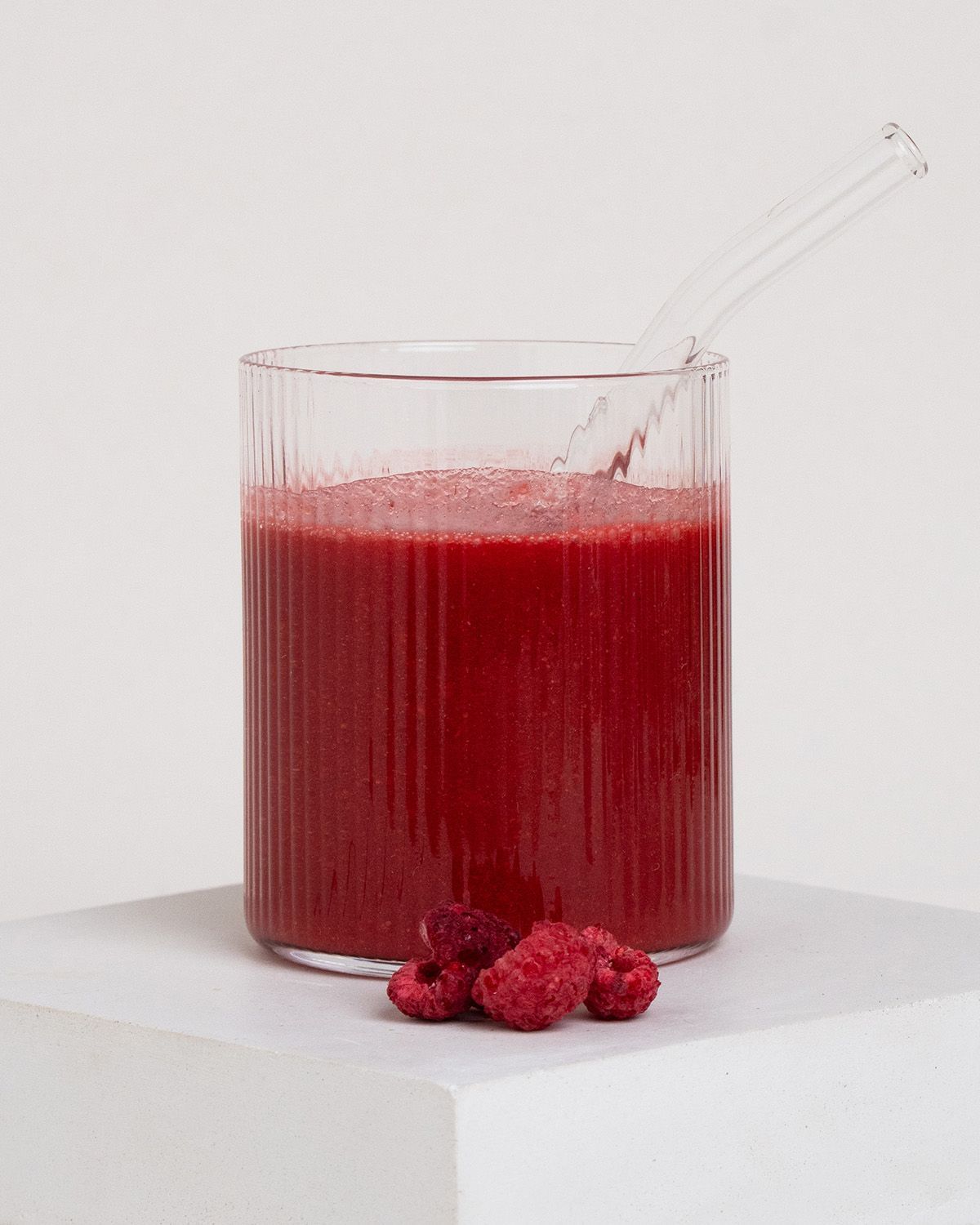 Ein Glas mit Himbeerpulver-Smoothie und frischen Himbeeren.