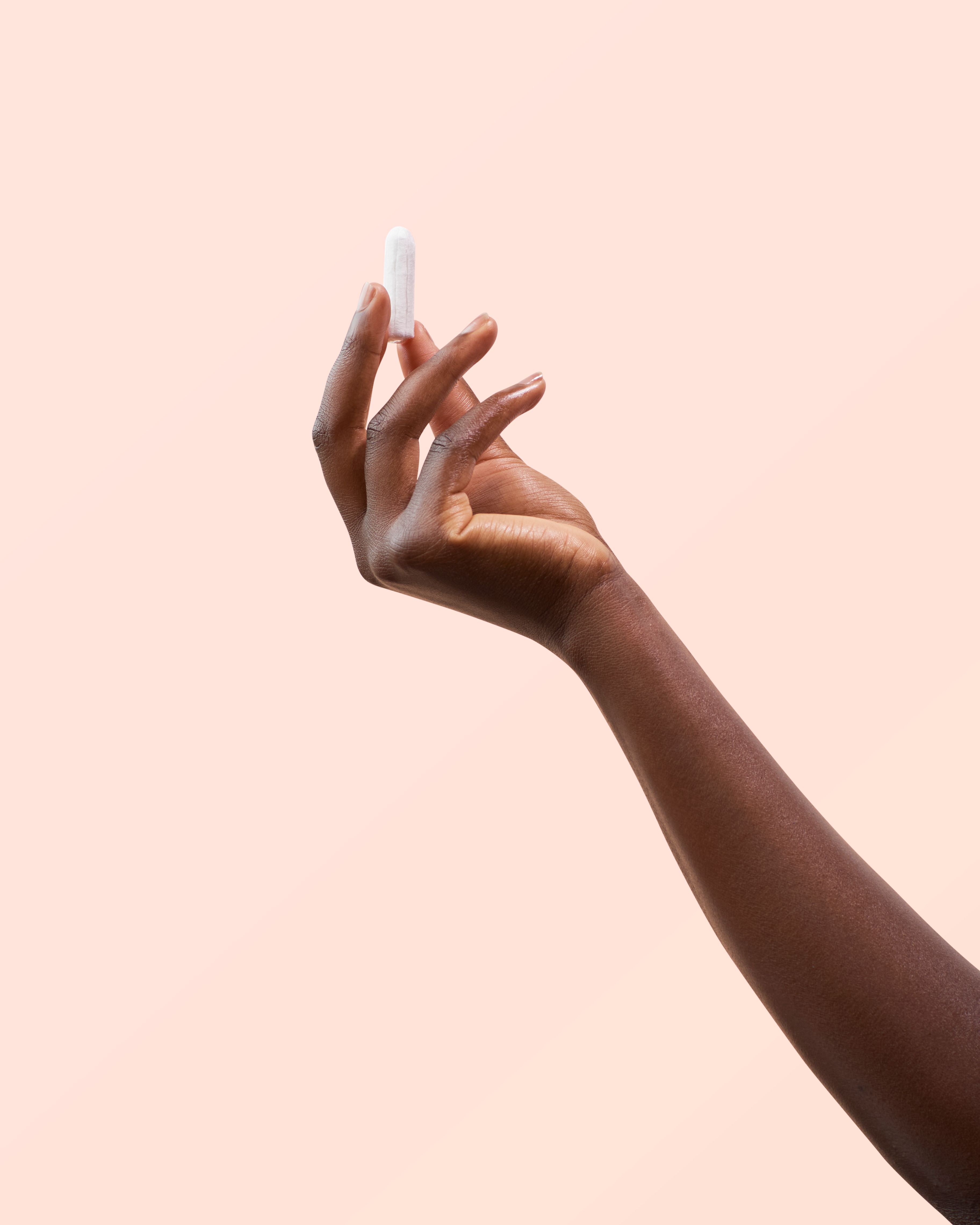 Eine Hand hält einen weißen Tampon. Hintergrund: Rosa.