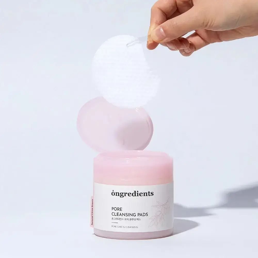 Hand hält Pad über Behälter mit "ongredients Pore Cleansing Pads". Rosa Deckel und Behälter. Weiße Pads.