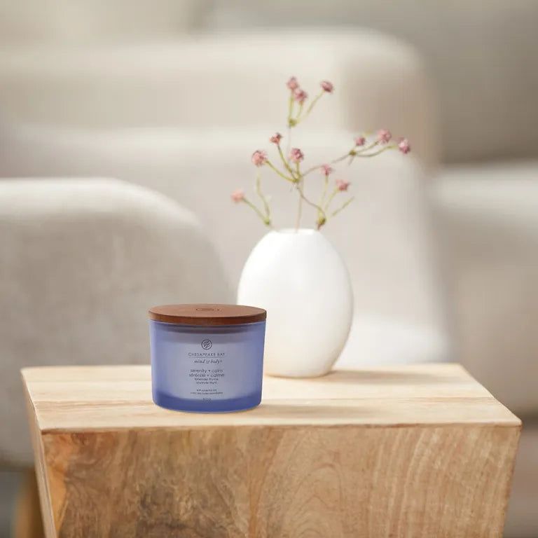 Blaue Kerze mit Holzdeckel. Aufschrift: 'Chesapeake Bay'. Steht auf einem Holztisch, neben einer Vase mit Blumen.