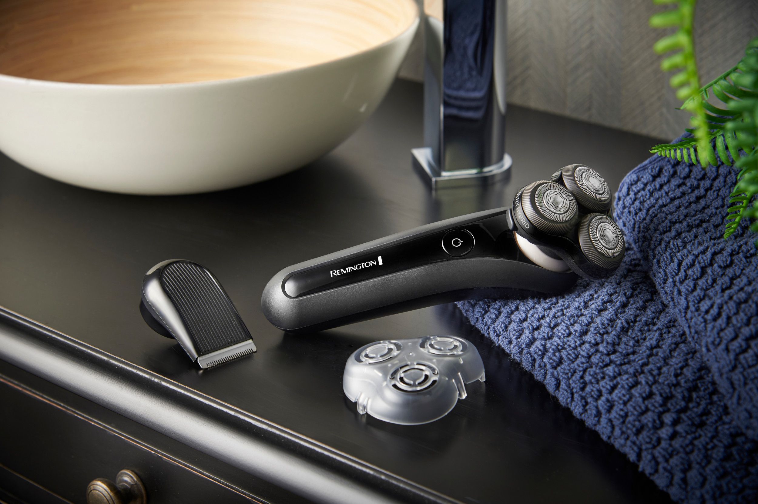 Schwarzer Rasierer mit Zubehör auf einer dunklen Oberfläche. Zubehör: Trimmeraufsatz und Ersatzscherkopf.