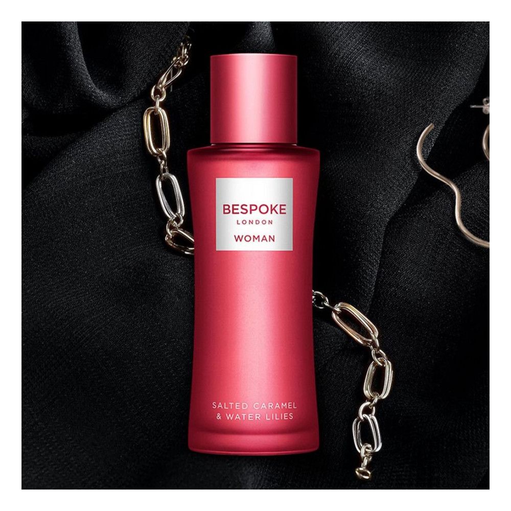 Rote Flasche auf schwarzem Stoff, umgeben von Schmuck. Aufschrift: Bespoke London Woman. Text: Salted Caramel & Water Lilies.