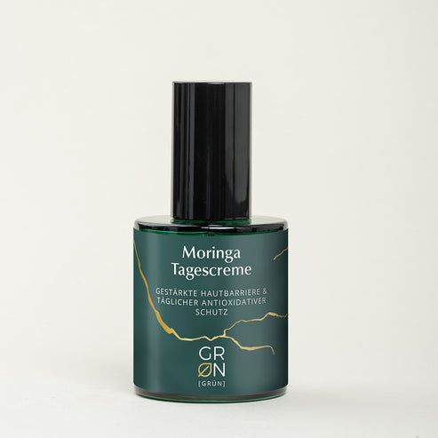 Grüne Glasflasche mit schwarzem Deckel. Aufschrift: Moringa Tagescreme. Goldene Linien.