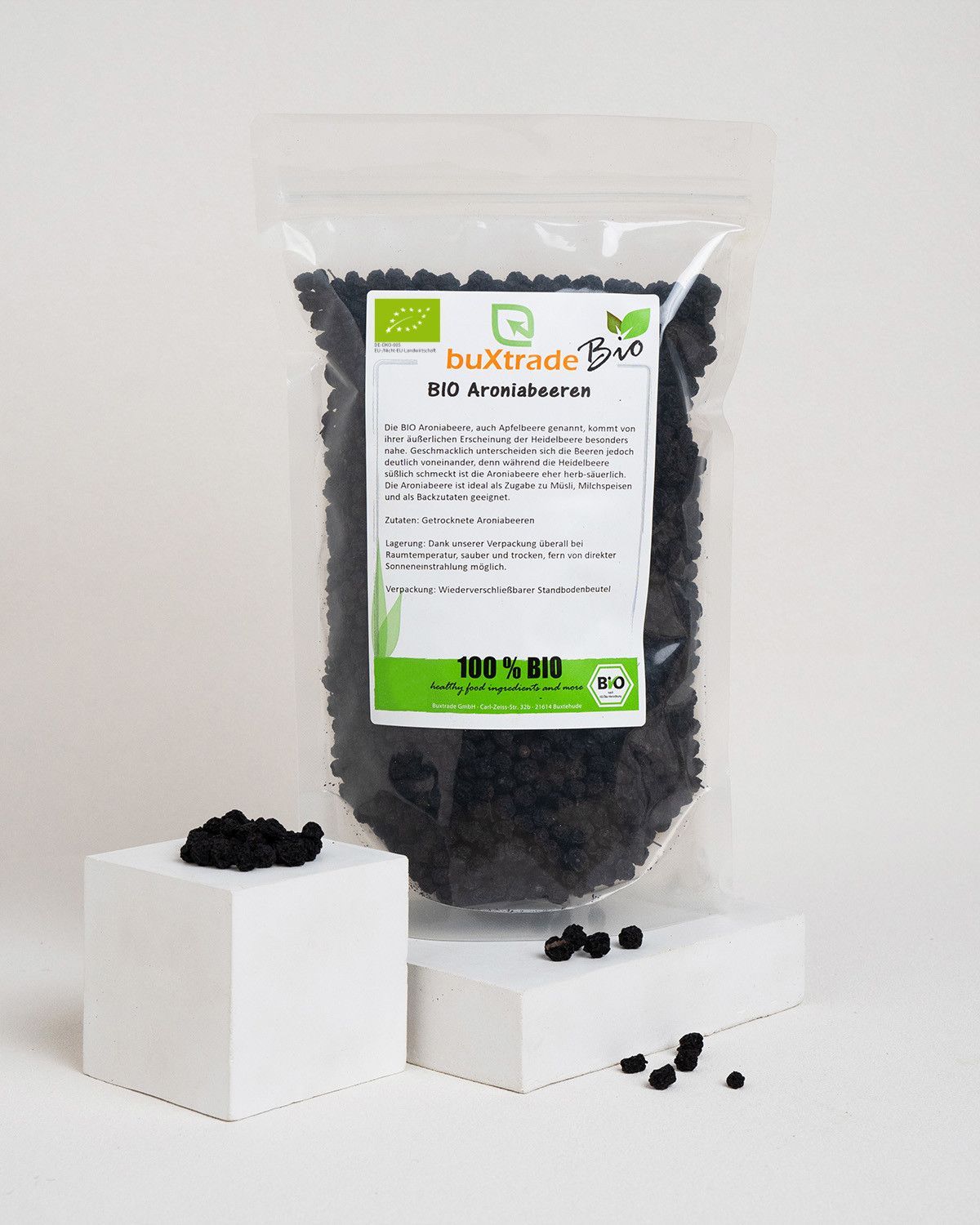 Verpackung mit BIO Aroniabeeren neben einem weißen Würfel mit Beeren.