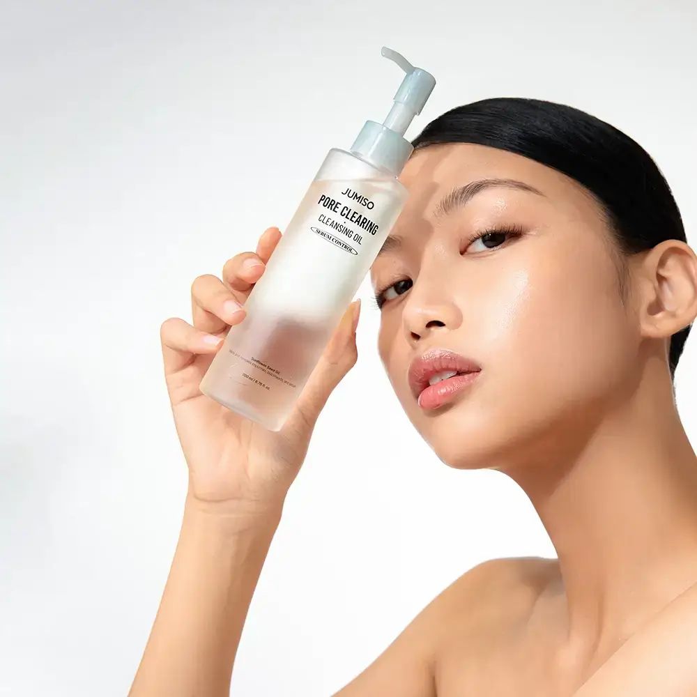 Frau hält eine Klarflasche mit Pumpe. Aufschrift: JUMISO PORE CLEARING CLEANSING OIL. Serum Control. Gesicht.