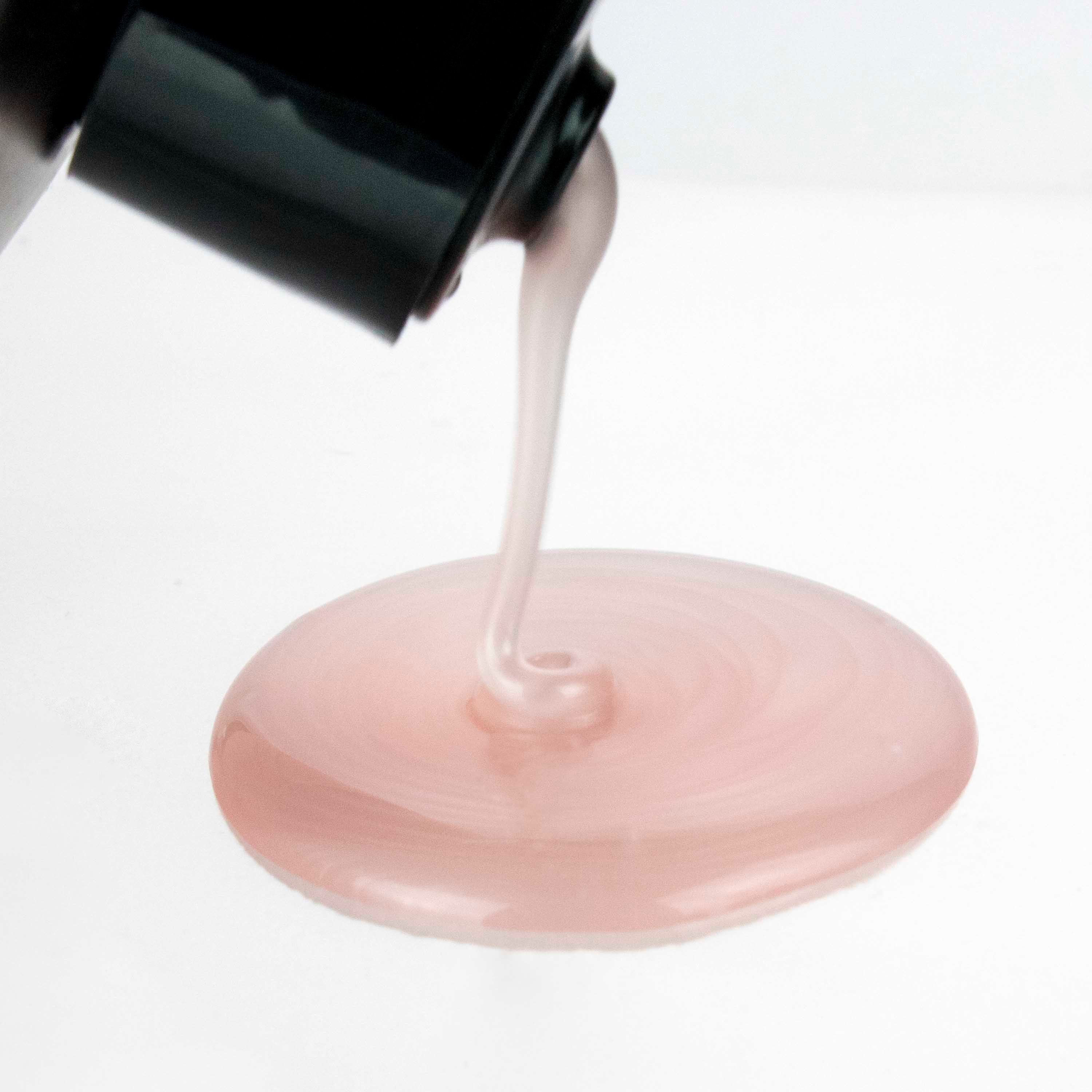 Rosa Shampoo fließt aus einer schwarzen Flasche. Der Hintergrund ist weiß. Die Flüssigkeit bildet einen kleinen See.