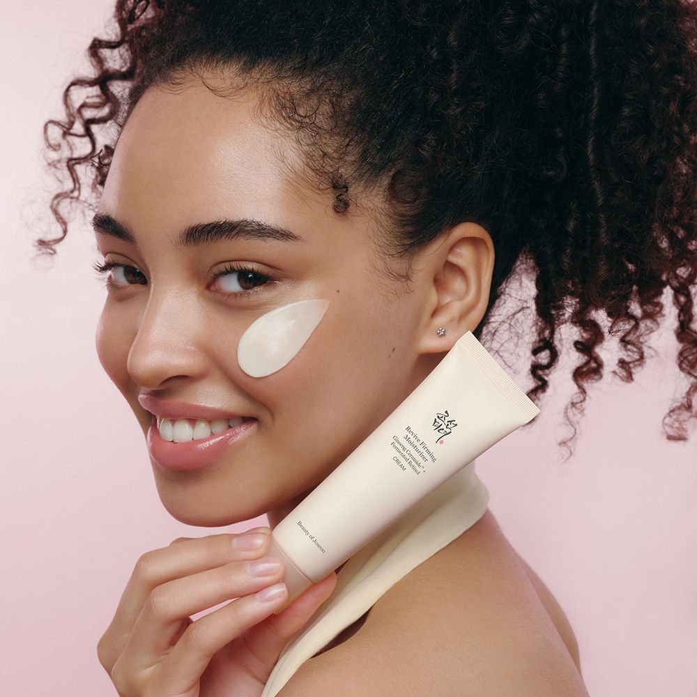 Frau hält eine Tube Beauty of Joseon Creme, mit Creme auf ihrer Wange.