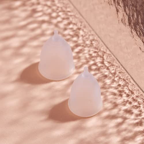 Zwei transparente Menstruationstassen auf rosa Untergrund. Beide haben eine runde Form mit Stiel.