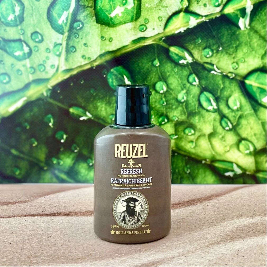 Reuzel Refresh No Rinse Bartwaschflasche vor einem Blatt mit Wassertropfen.