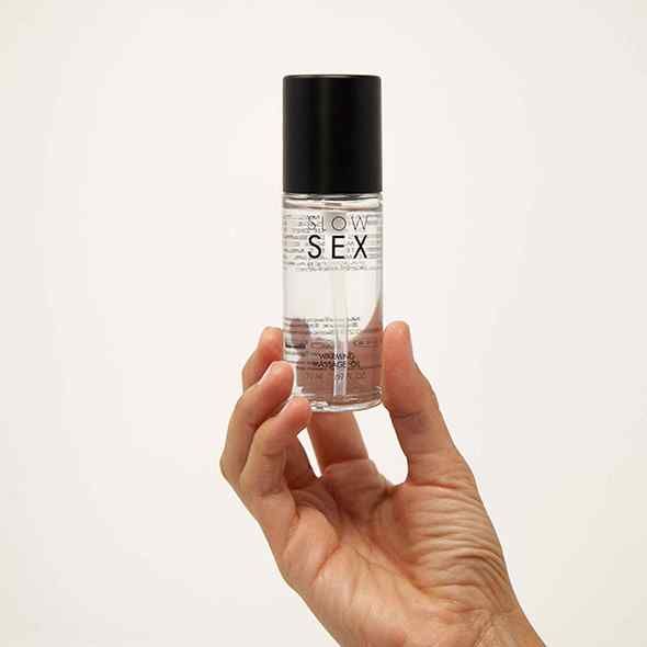Hand hält eine Flasche Massageöl. Aufschrift: SLOW SEX. Bezeichnung: Warming Massage Oil. Schwarzer Deckel, transparente Flüssigkeit.