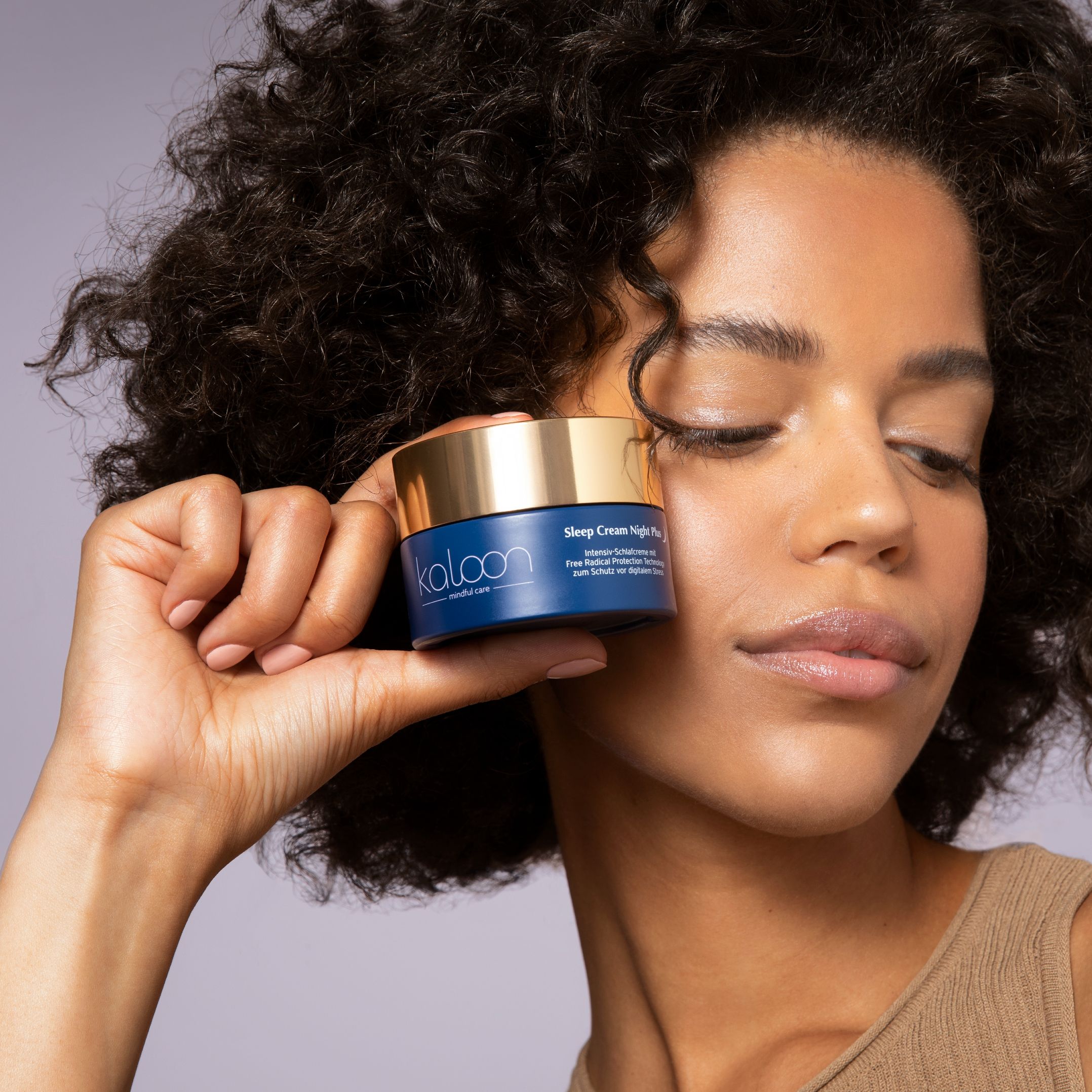 Frau hält blaue Creme-Dose mit goldenem Deckel. Aufschrift: KALOON, Sleep Cream Night Plus. Gesicht.