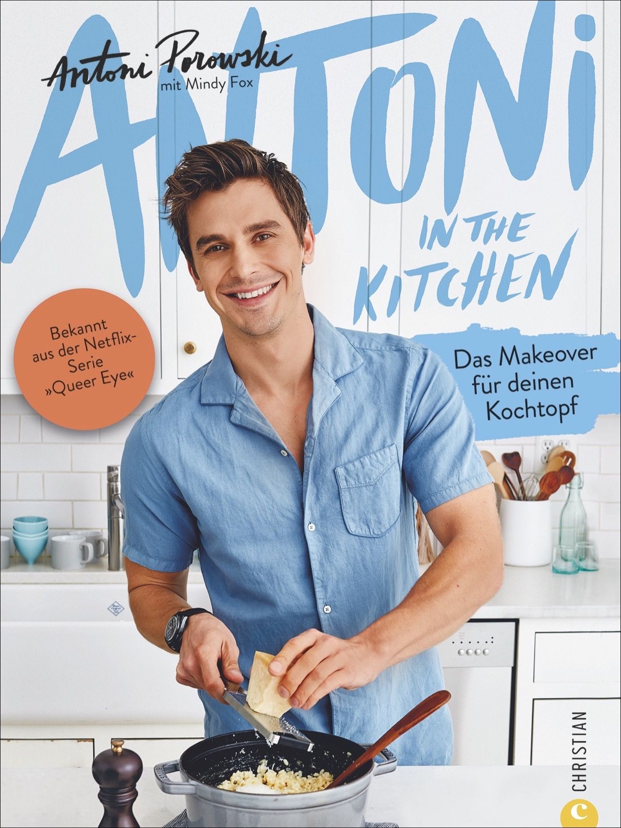 Buchcover: Antoni in the Kitchen. Antoni Porowski lächelt. Titel in blau. Orangefarbener Kreis mit Text. Kochtopf und Zutaten im Vordergrund.
