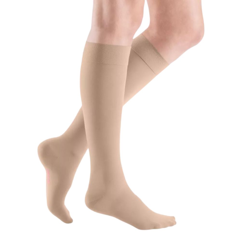 Beige Kompressions-Kniestrümpfe an Beinen. Blick von der Seite, auf weißem Hintergrund. Strümpfe reichen bis unterhalb des Knies.