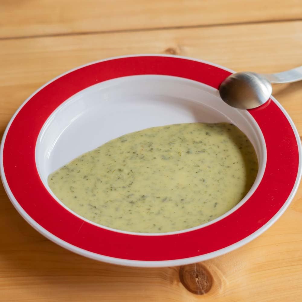 Teller mit rotem Rand, gefüllt mit Suppe und Löffel.