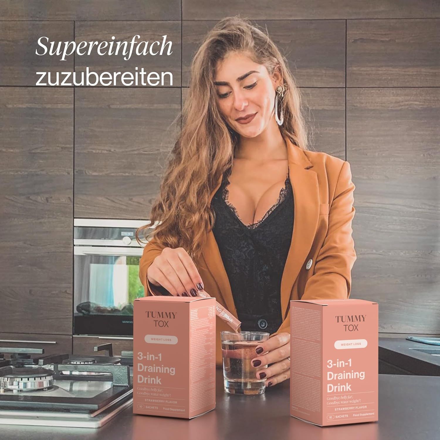 Frau in Küche hält zwei Packungen "Tummy Tox 3-in-1 Draining Drink" und ein Glas Wasser.