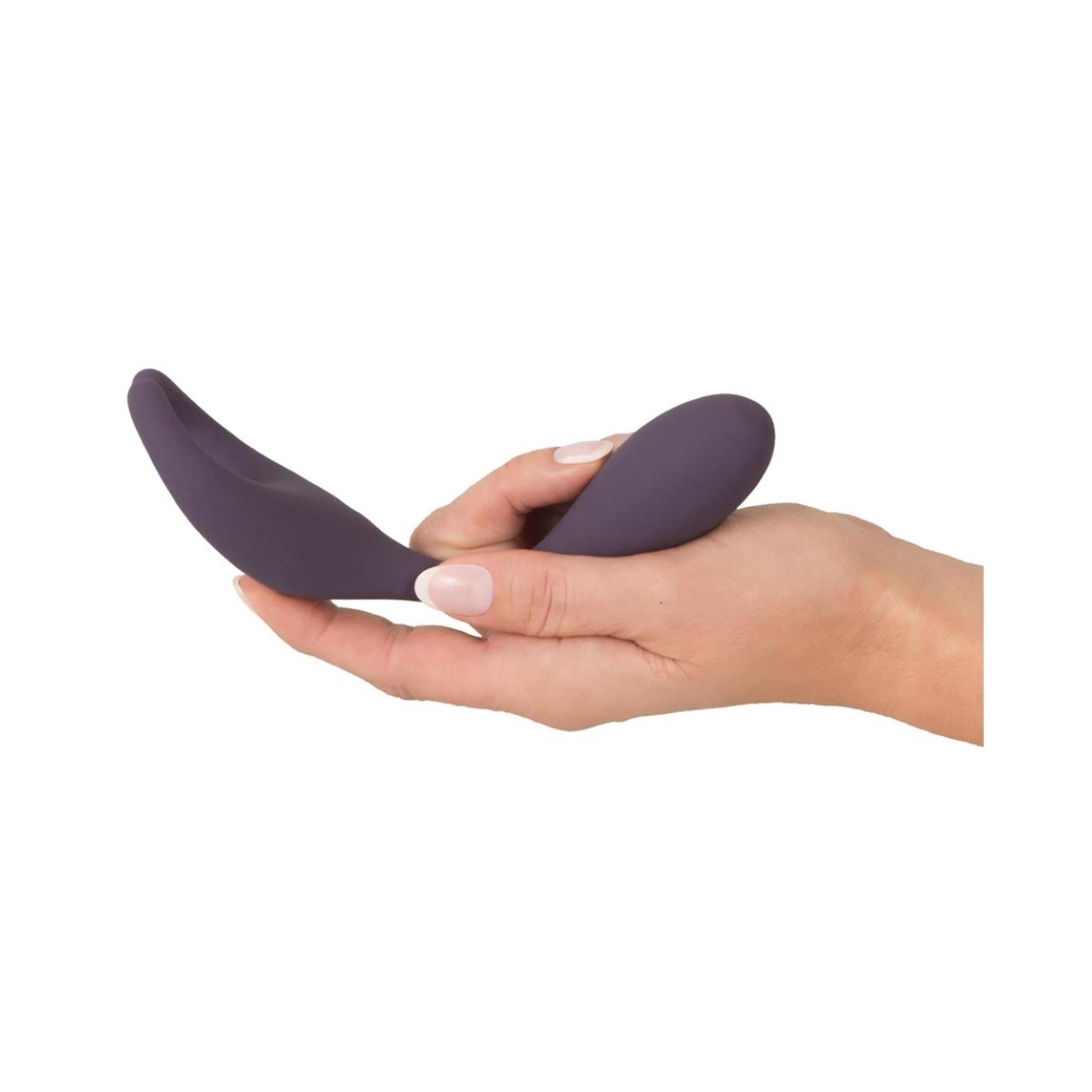 Hand hält lila Vibrator. Geschwungene Form. Glatte Oberfläche. Tropfenförmiger Griff.