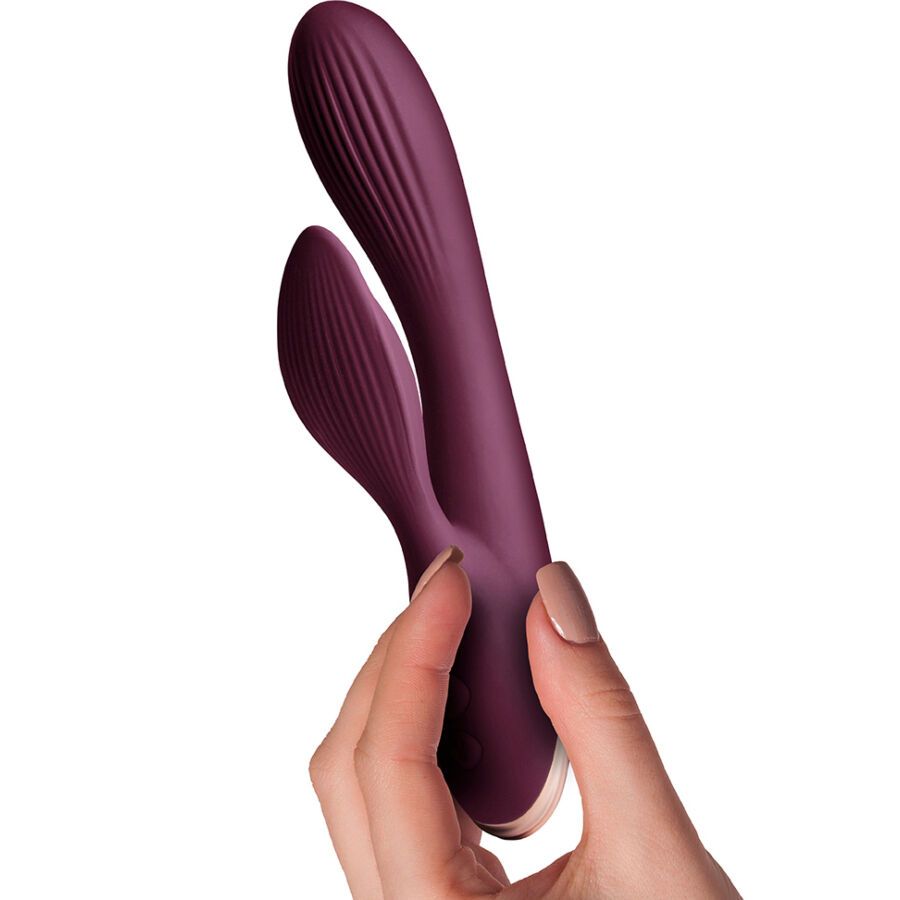 Lila Vibrator mit geriffelter Oberfläche, gehalten von einer Hand. Goldfarbener Sockel.