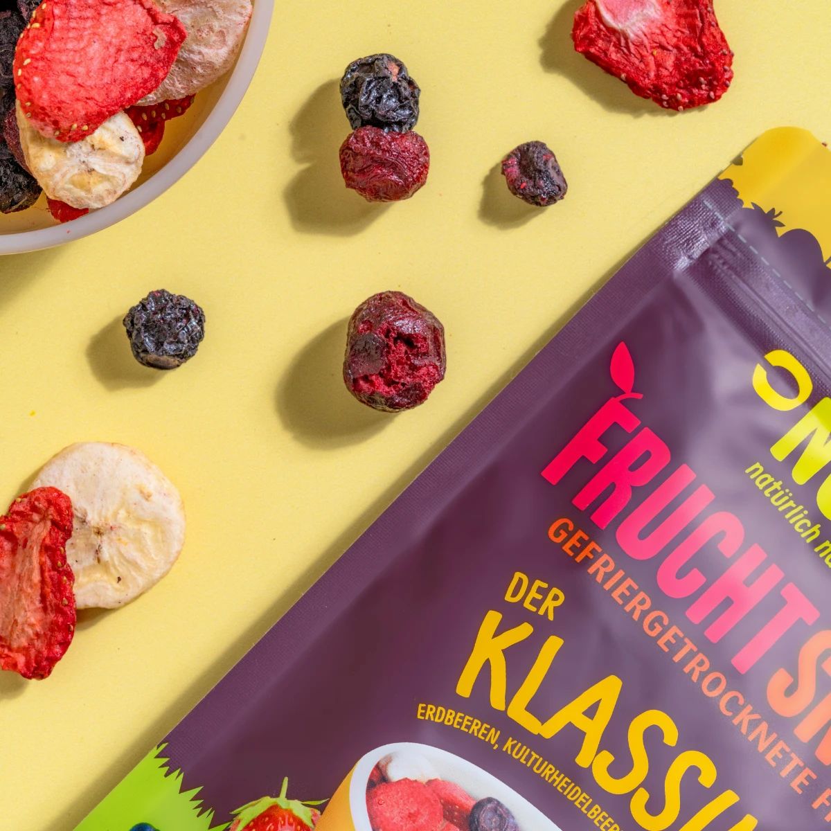 Nahaufnahme von gefriergetrockneten Früchten und einer Packung. Aufschrift: NutriPur, Frucht Snacks, Der Klassiker.