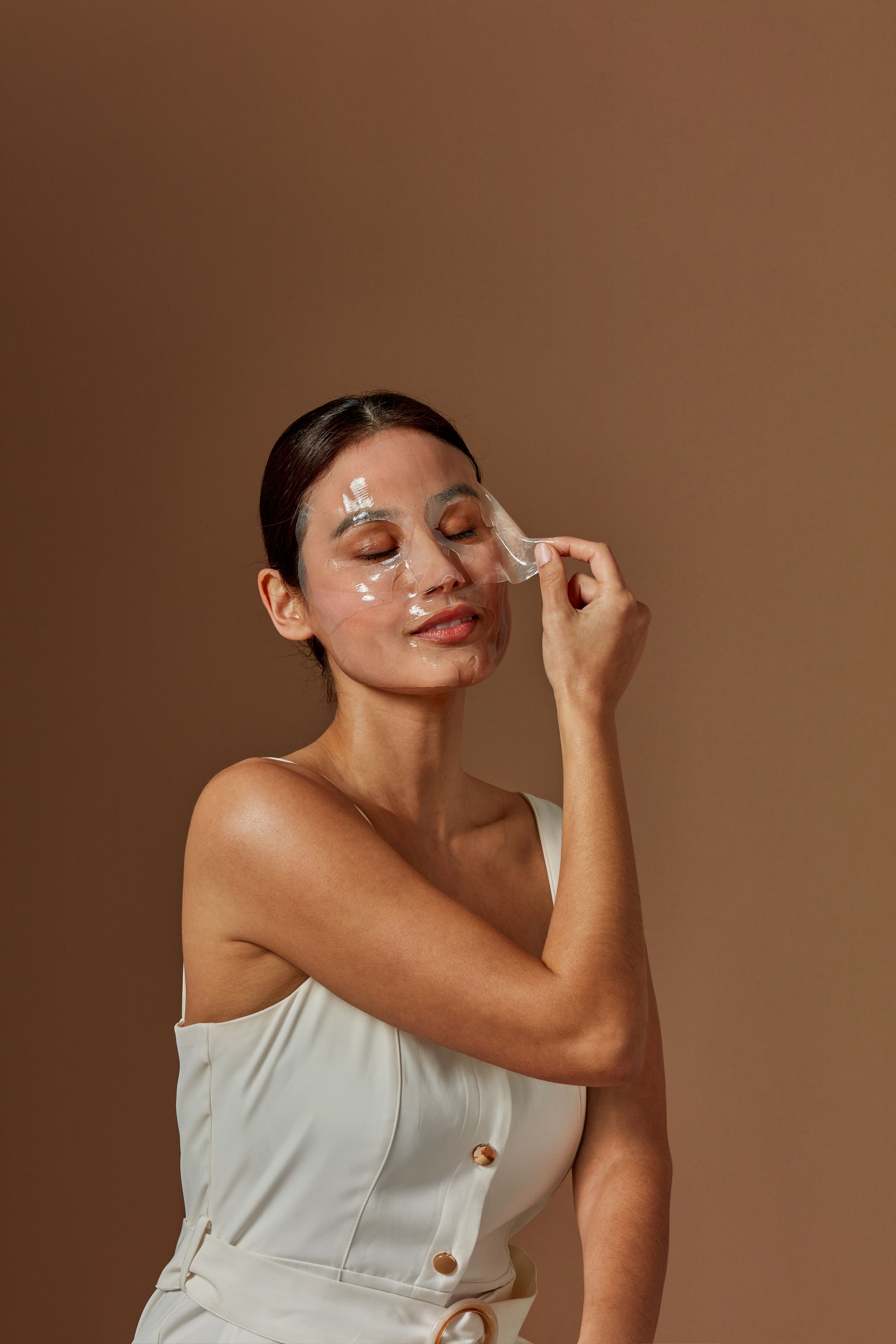 Frau mit geschlossenen Augen, hält eine transparente Hydrogel-Gesichtsmaske. Die Maske bedeckt Teile des Gesichts.
