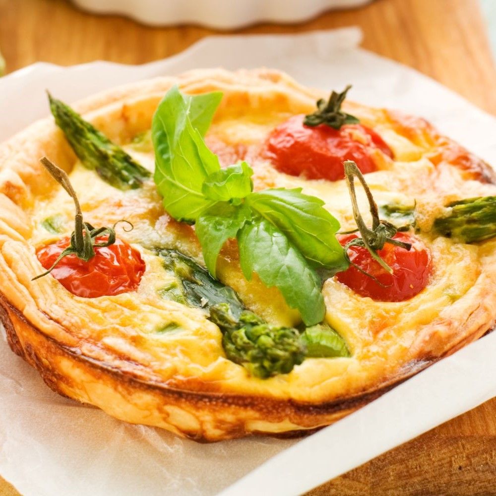 Quiche mit Tomaten, Spargel und Basilikum. Auf einem Holzbrett. Nahaufnahme.
