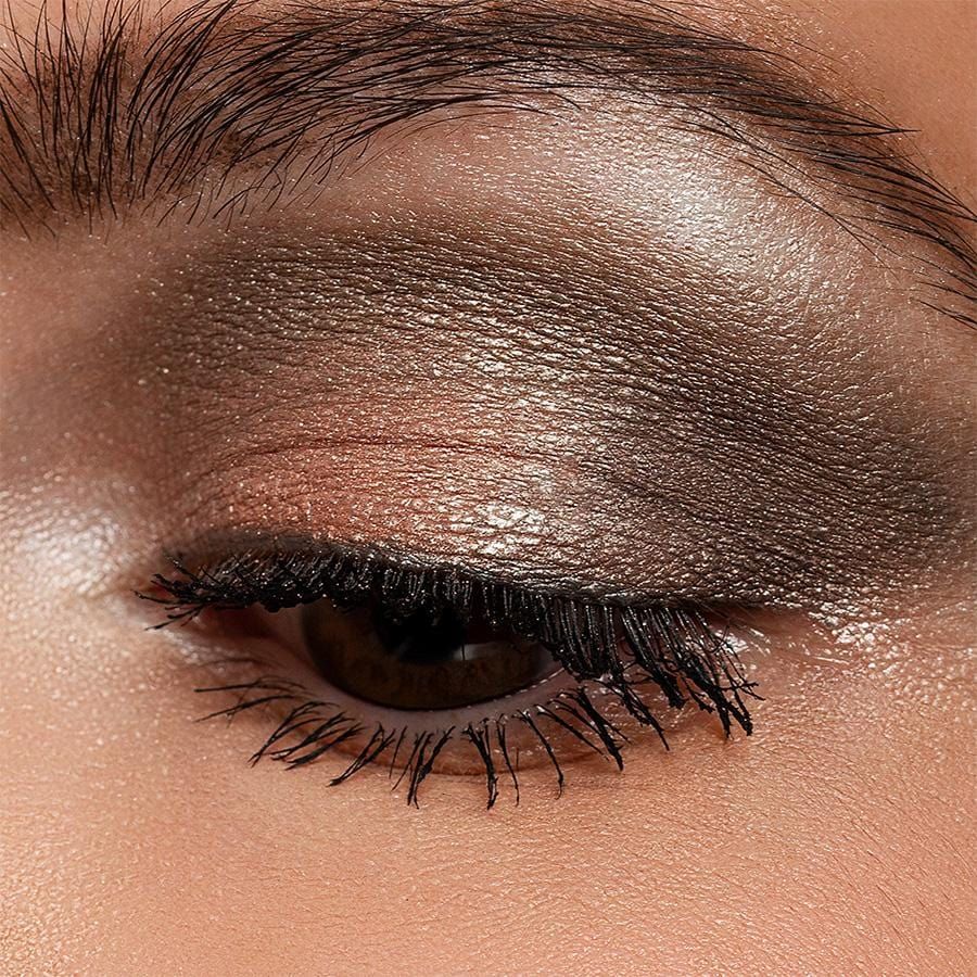 Auge mit Lidschatten. Farben: Gold, Braun. Wimpern getuscht. Hauttextur sichtbar.