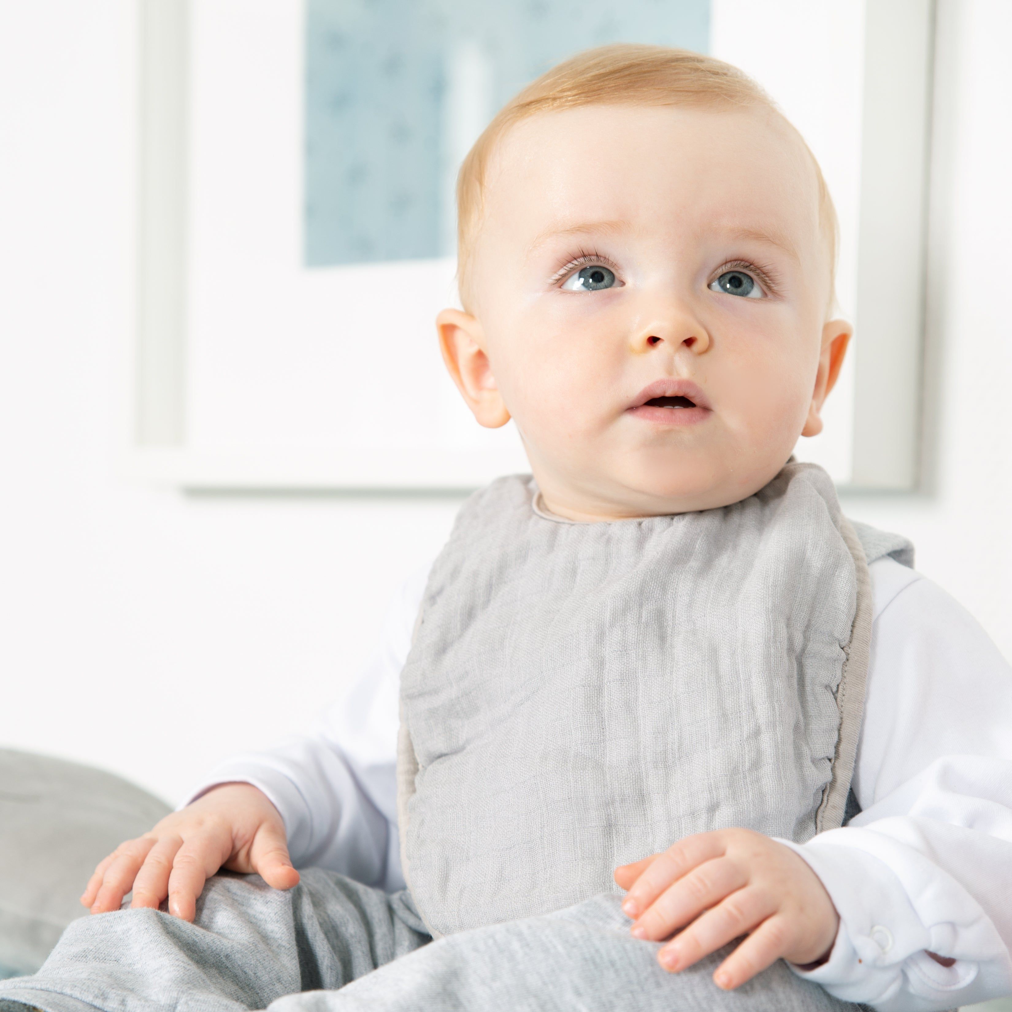 Baby mit grauem Lätzchen. Das Kind blickt nach oben.