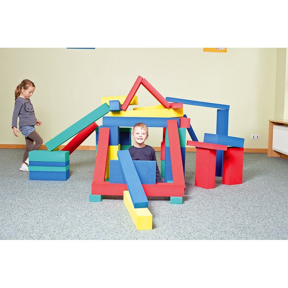 Kinder spielen mit bunten Schaumstoffquadern. Sie bauen eine Struktur. Farben: blau, rot, gelb, grün.