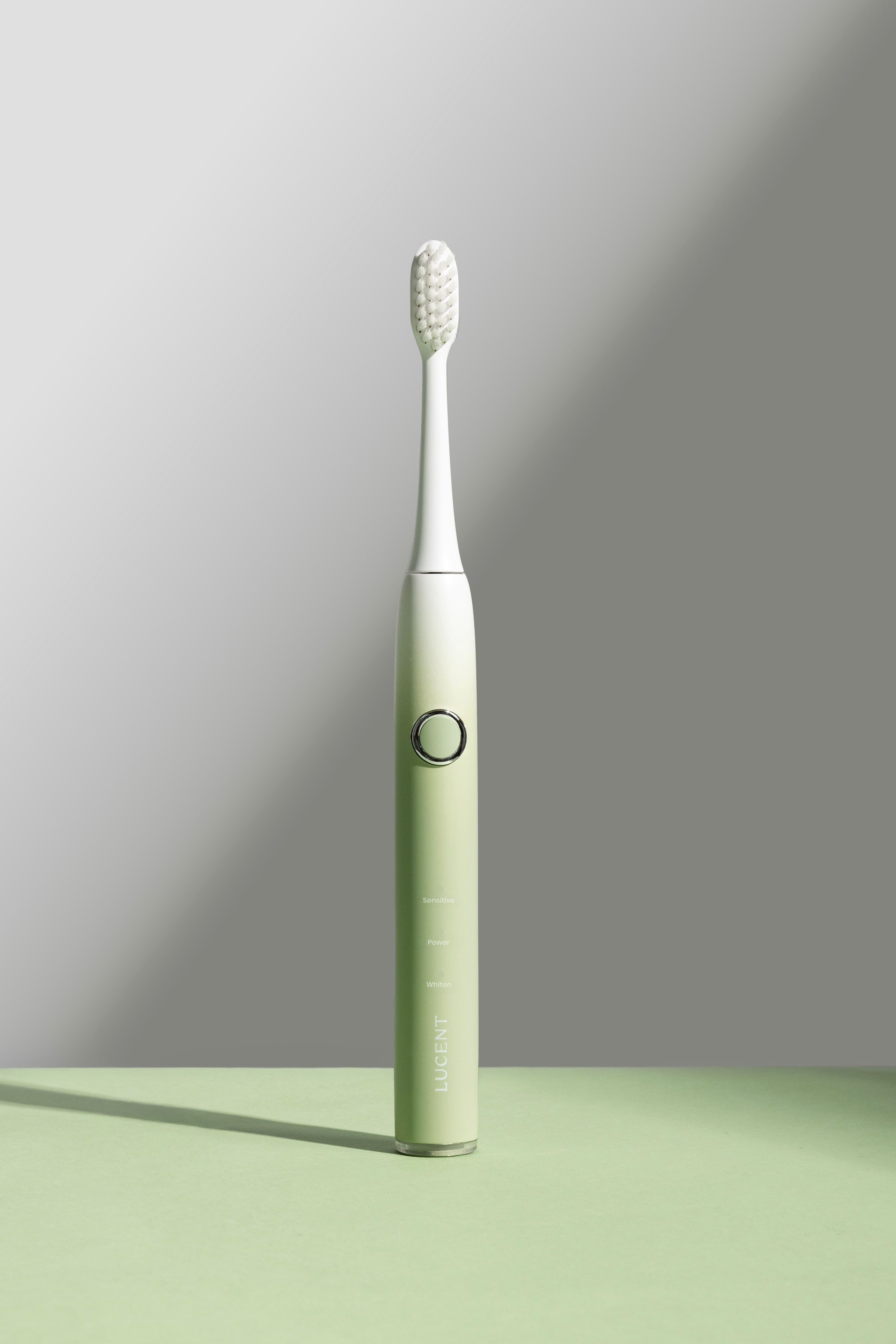 Elektrische Zahnbürste mit grünem Griff und weißem Bürstenkopf. Knopf und Schriftzug sichtbar. Schatten.
