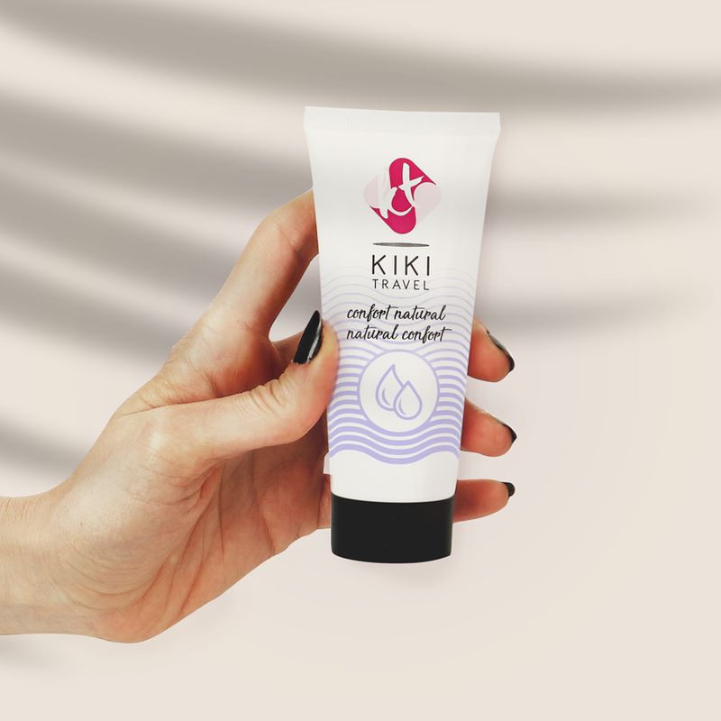 Hand hält Tube Gleitgel. Aufschrift: KIKI TRAVEL, confort natural. Weiße Tube mit lila Akzenten und schwarzem Verschluss.