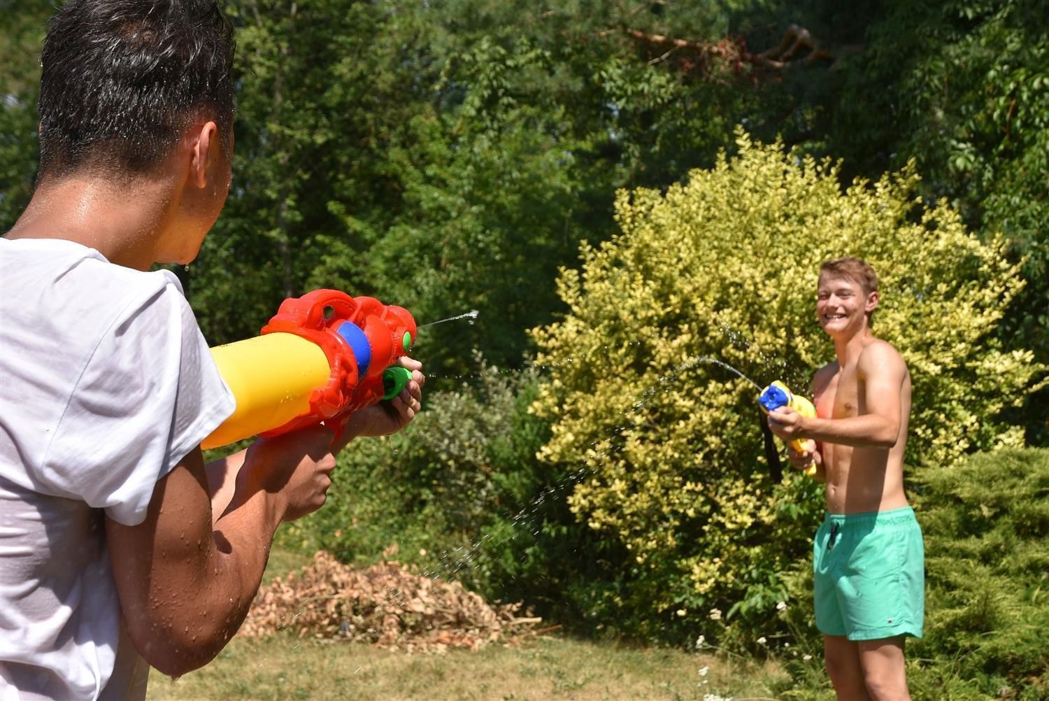 Zwei Männer spielen mit Wasserpistolen im Freien. Eine Person hält eine rote und gelbe Pistole. Die andere Person hält eine blaue Pistole.