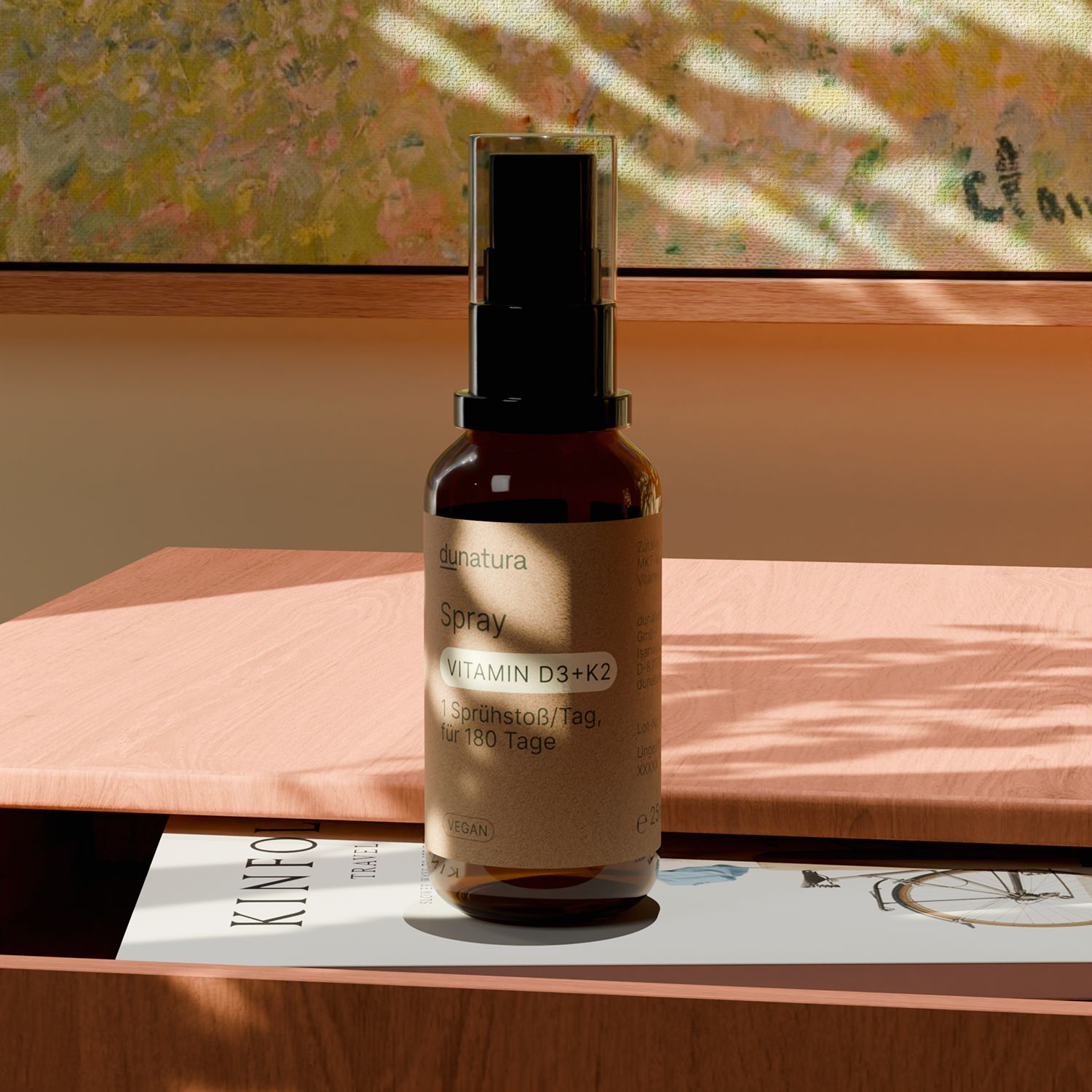 Braune Glasflasche mit schwarzem Sprühkopf auf einem Tisch. Etikett mit "dunatura Spray Vitamin D3+K2".