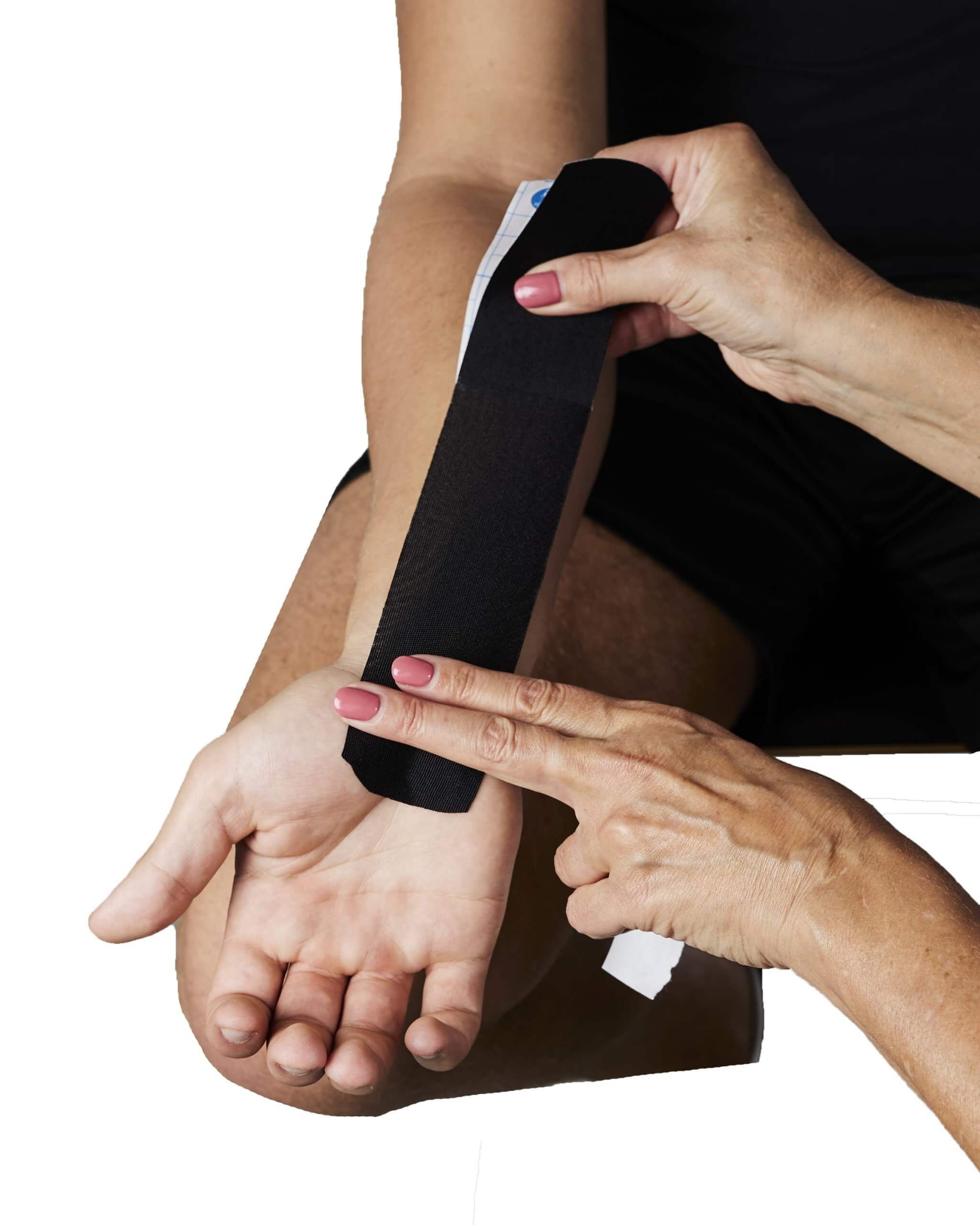 Hände bringen schwarzes Kinesiotape an einem Unterarm an. Tape wird auf die Haut geklebt. Hautfarbe sichtbar.