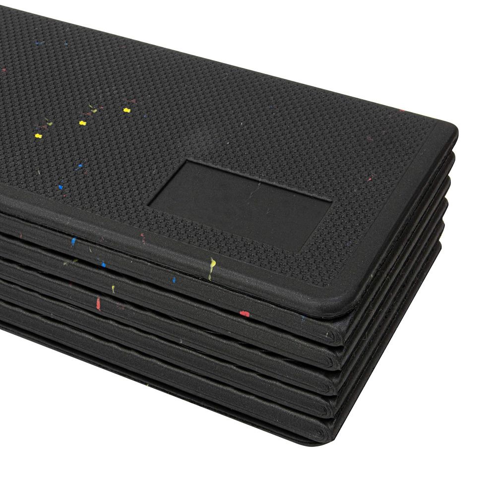 Gefaltete, schwarze Fitnessmatte mit farbigen Spritzern. Rechteckige Form, geriffelte Oberfläche. Mehrere Schichten sichtbar.