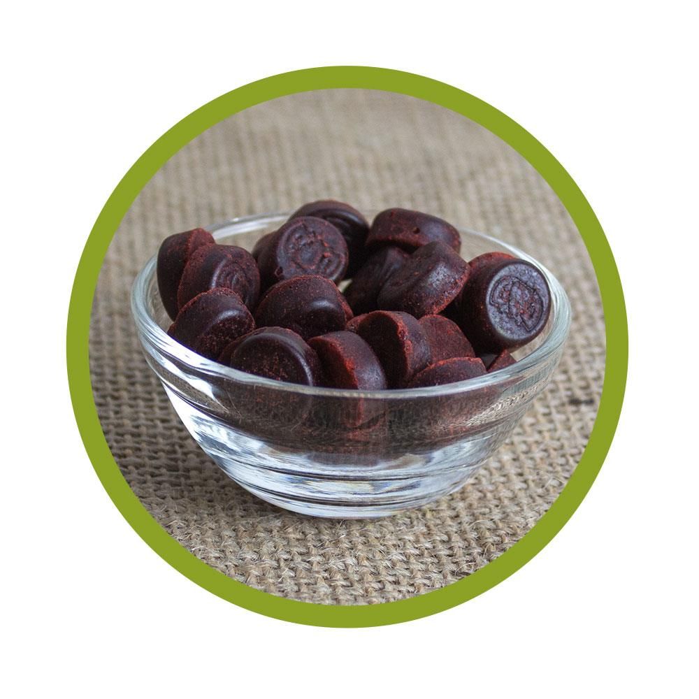 Runde, dunkelrote Bonbons in einer Glasschale. Auf einigen Bonbons ist ein Prägedruck zu sehen.