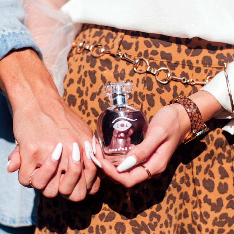 Zwei Hände halten einen Flakon. Der Flakon hat rosa Flüssigkeit, silbernen Hals und transparenten Deckel. Aufschrift "EOL" und "MORNING GLOW".