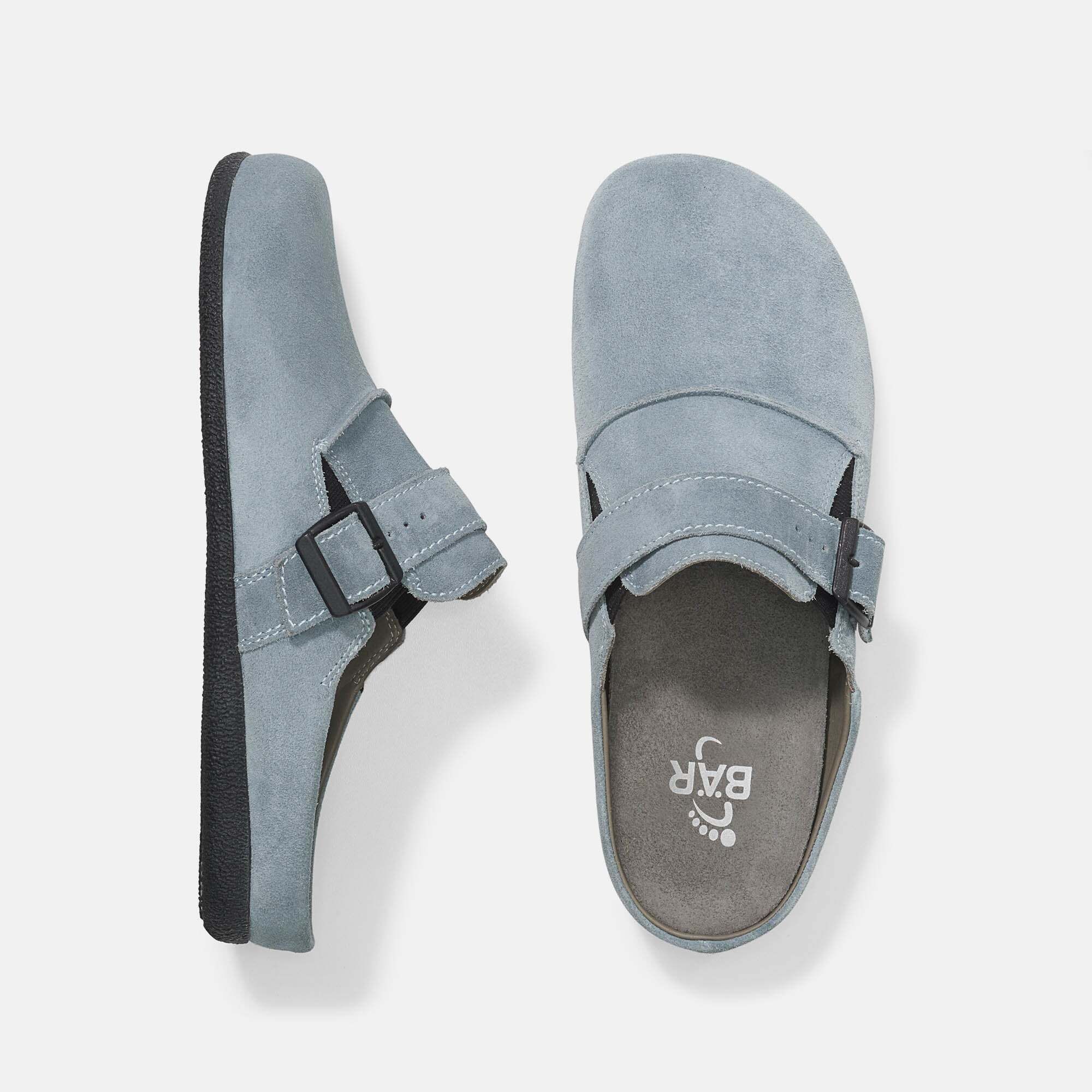 Draufsicht auf zwei hellblaue Pantoletten. Schwarze Sohle, helles Innenfutter. Logo auf der Innensohle.