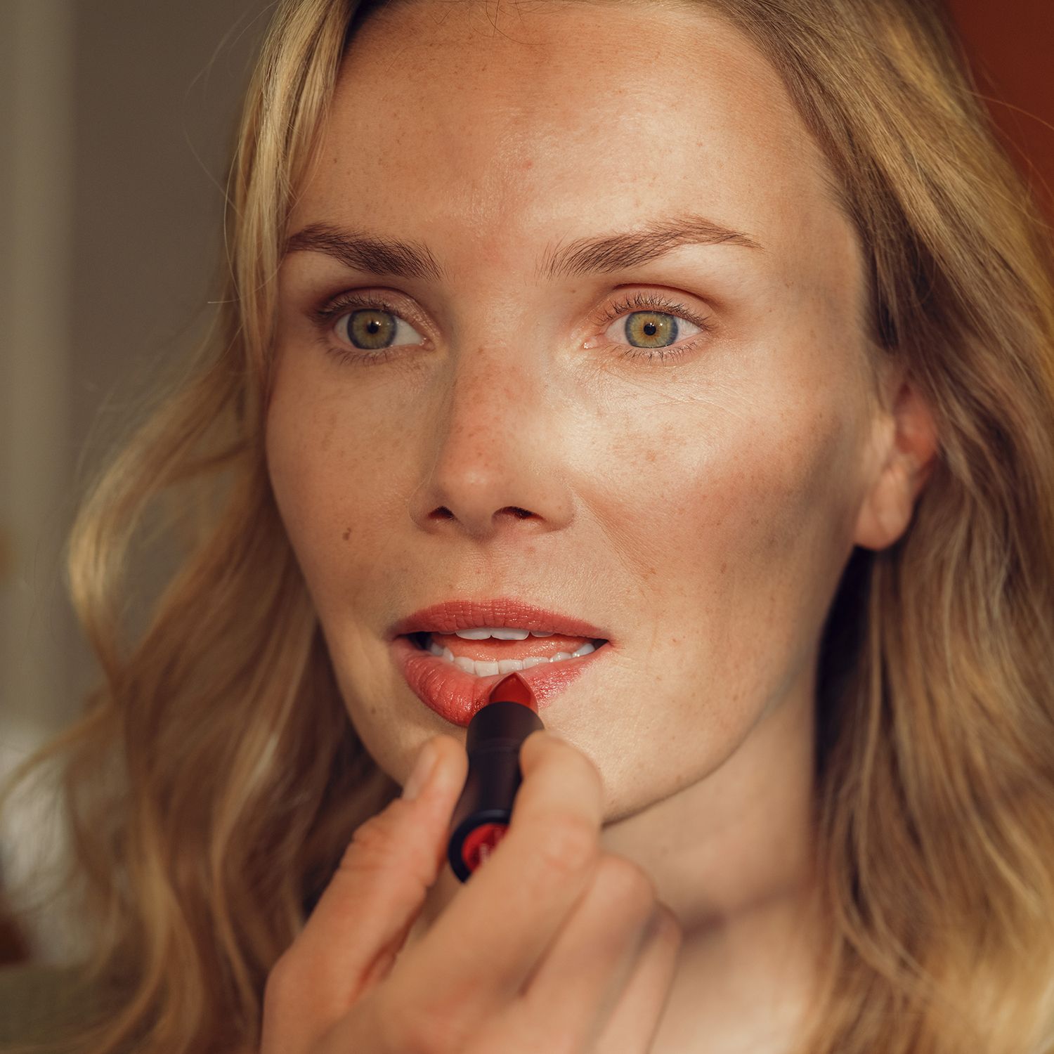 Frau trägt roten Lippenbalsam auf. Schwarzer Lippenbalsam im Bild. Gesicht und Lippen sind im Fokus.